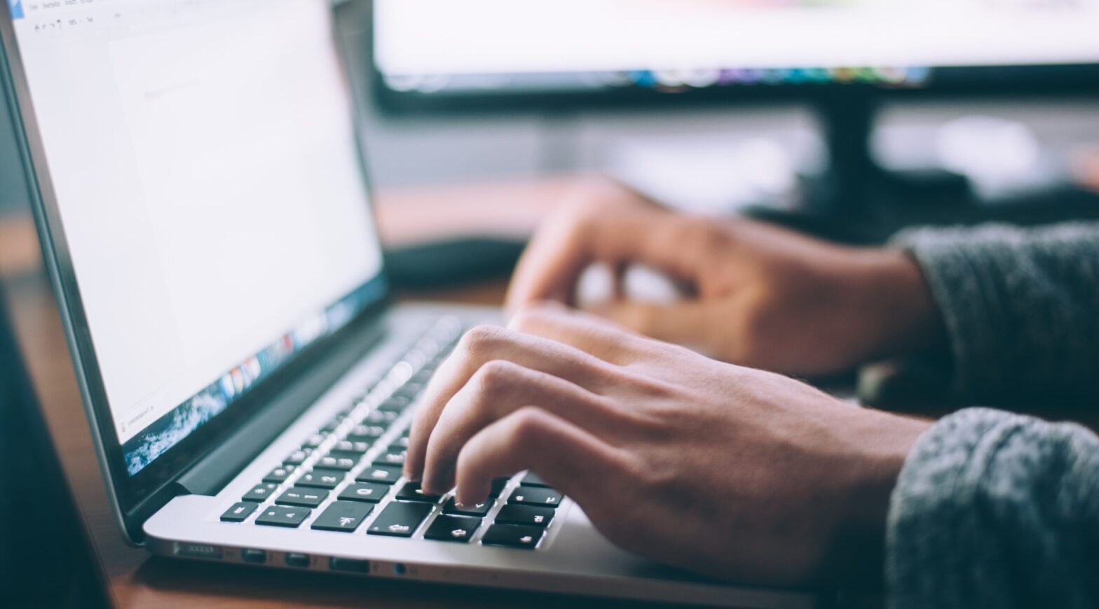 Zbliżenie na dłonie mężczyzny piszące na laptopie.