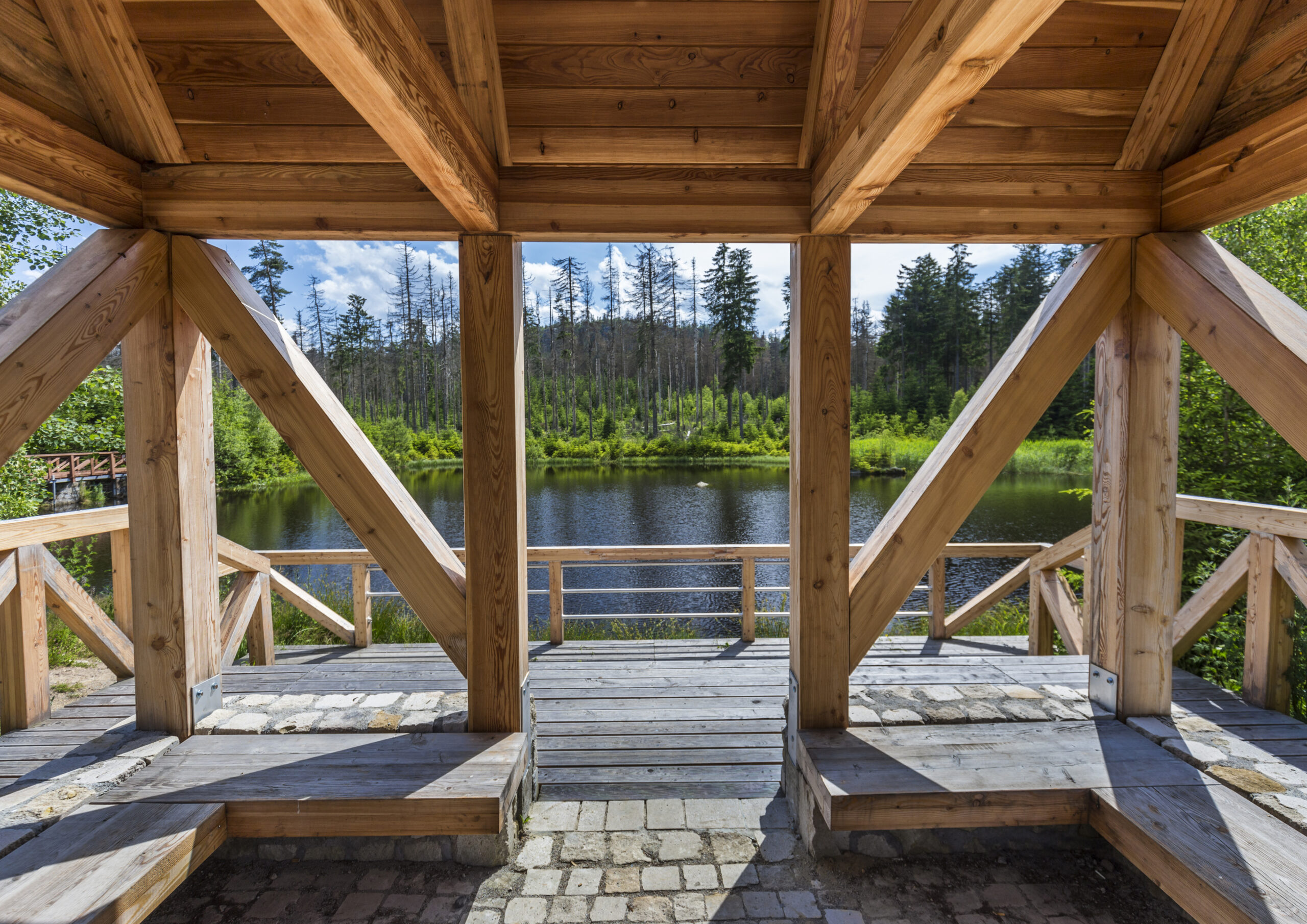 Drewniana wiata turystyczna z ławkami do odpoczynku i z tarasem widokowym w Parku Narodowym Gór Stołowych. Widok z wnętrza wiaty na jezioro i las. Pogodny dzień.